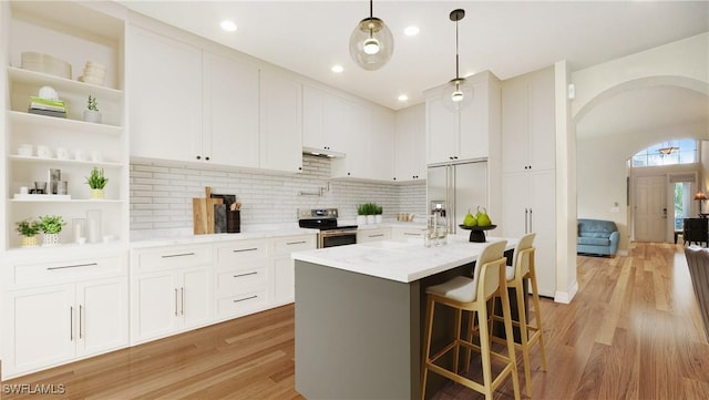 kitchen with tasteful backsplash, white cabinetry, pendant lighting, stainless steel appliances, and a center island with sink