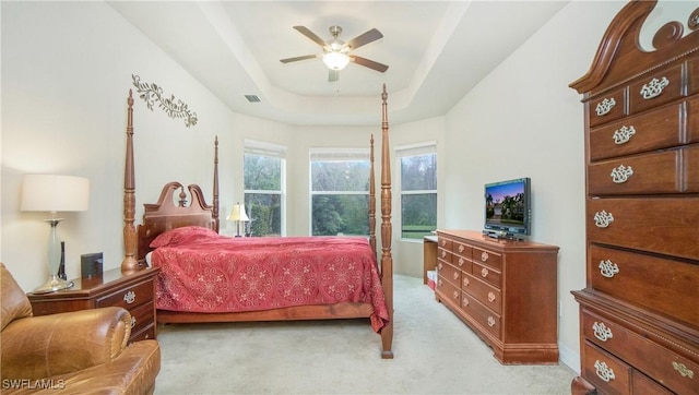 bedroom with ceiling fan, a tray ceiling, and light carpet