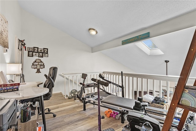 exercise area featuring a textured ceiling, light hardwood / wood-style flooring, and lofted ceiling with skylight