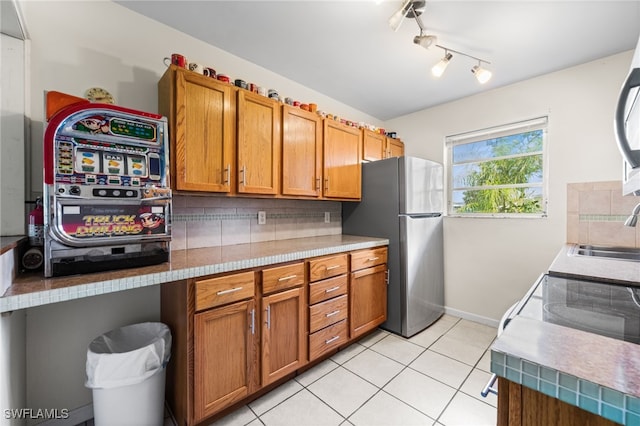 kitchen featuring decorative backsplash, light tile patterned floors, sink, and stainless steel refrigerator