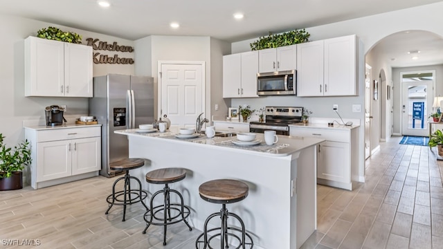 kitchen featuring white cabinets, an island with sink, stainless steel appliances, and light wood-type flooring