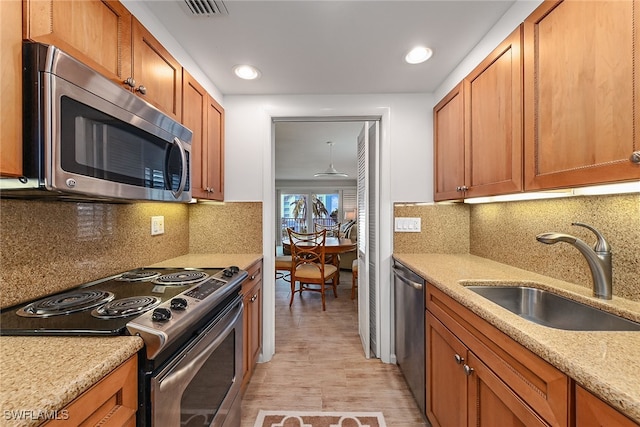 kitchen with light stone counters, appliances with stainless steel finishes, decorative backsplash, sink, and light hardwood / wood-style flooring