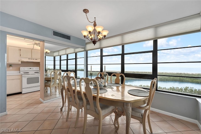 tiled dining room with ceiling fan with notable chandelier, a wealth of natural light, and a water view