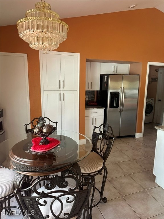 dining area with a chandelier, washer / clothes dryer, lofted ceiling, and light tile patterned floors