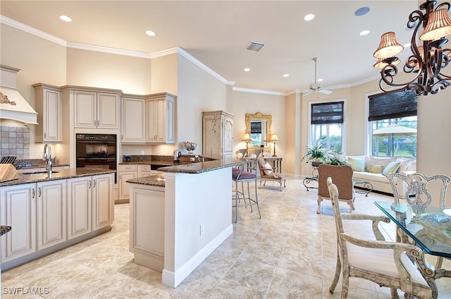 kitchen with sink, double oven, dark stone countertops, crown molding, and cream cabinetry