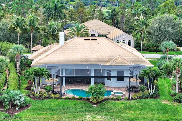 back of house featuring a lanai, a swimming pool with hot tub, a patio area, and a lawn