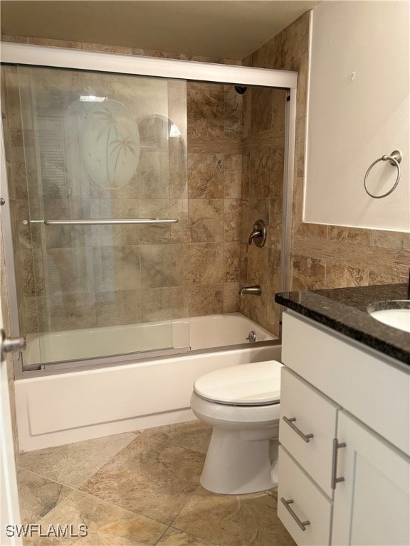 full bathroom featuring combined bath / shower with glass door, vanity, toilet, and tile walls