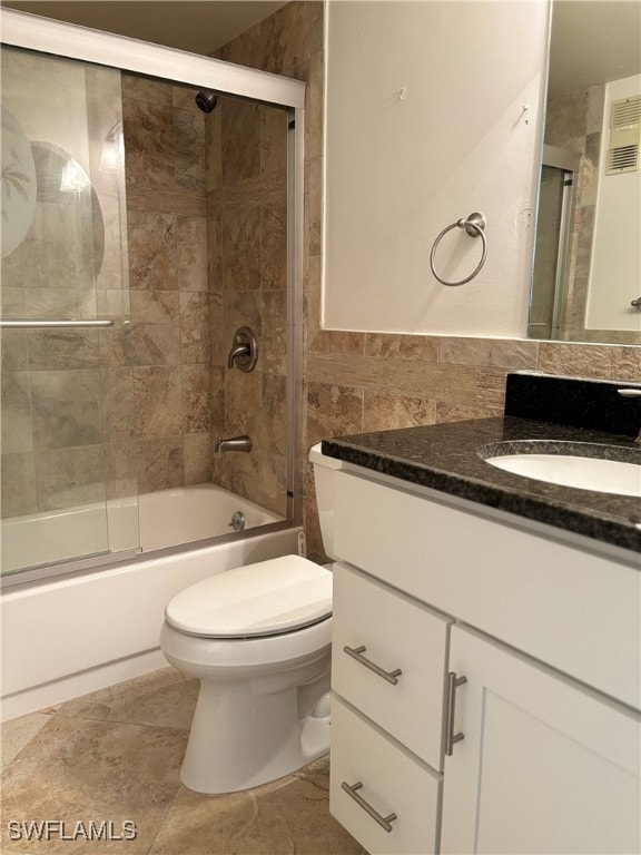 full bathroom featuring vanity, shower / bath combination with glass door, tile patterned floors, toilet, and tile walls