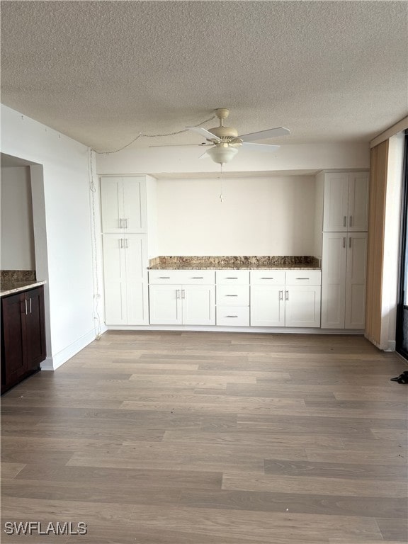 kitchen featuring light wood-type flooring, light stone counters, a textured ceiling, ceiling fan, and white cabinetry