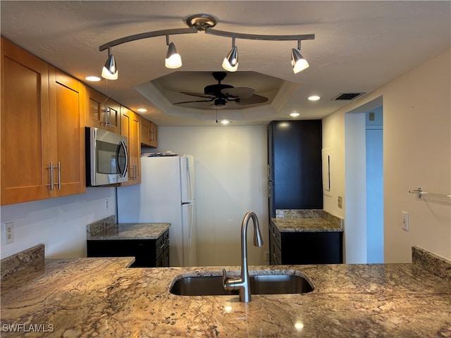 kitchen with ceiling fan, a raised ceiling, light stone countertops, and sink