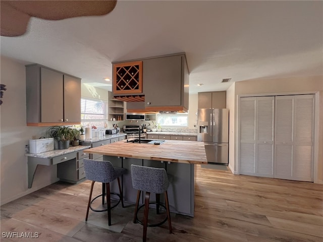 kitchen with sink, gray cabinetry, wood counters, light wood-type flooring, and appliances with stainless steel finishes