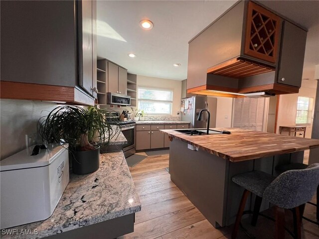 kitchen with light wood-type flooring, appliances with stainless steel finishes, gray cabinets, sink, and kitchen peninsula