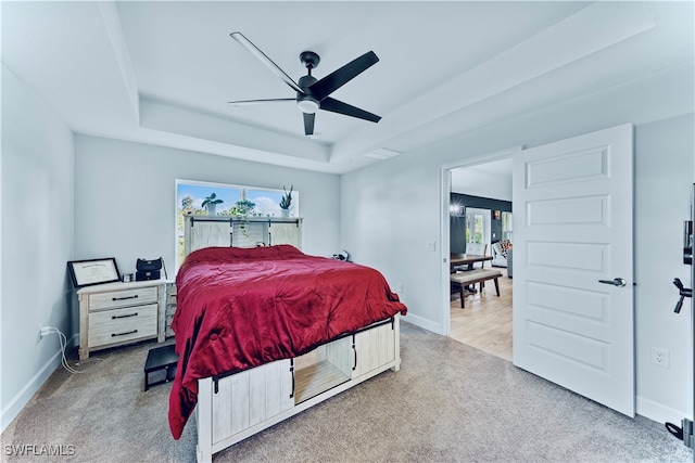 bedroom featuring ceiling fan, a raised ceiling, and light colored carpet