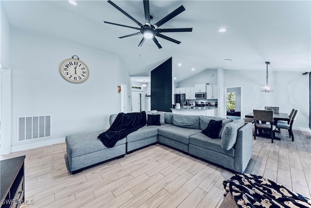 living room with light wood-type flooring, ceiling fan, sink, and vaulted ceiling