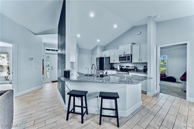 kitchen featuring stainless steel appliances, white cabinetry, stone countertops, a kitchen breakfast bar, and light hardwood / wood-style flooring