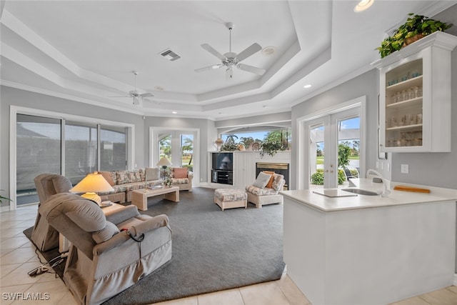 tiled living room with french doors, ceiling fan, crown molding, and a tray ceiling