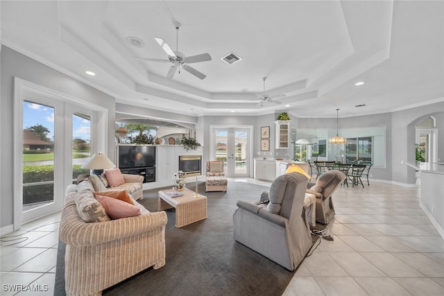 tiled living room featuring crown molding, french doors, ceiling fan, and a raised ceiling