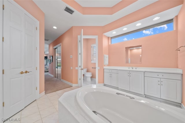 bathroom with a relaxing tiled tub, vanity, and toilet