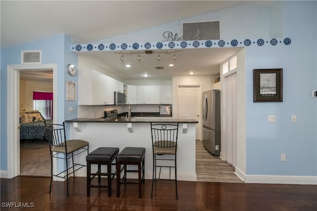 kitchen featuring kitchen peninsula, stainless steel appliances, vaulted ceiling, white cabinets, and dark hardwood / wood-style floors