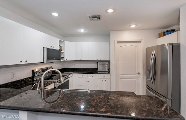 kitchen with kitchen peninsula, appliances with stainless steel finishes, white cabinetry, and dark stone countertops