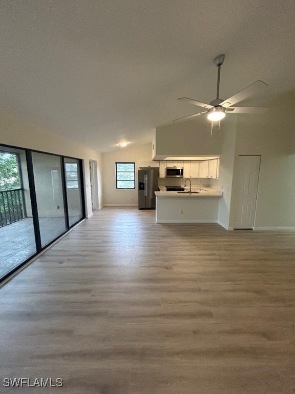 unfurnished living room with light hardwood / wood-style flooring, sink, ceiling fan, and vaulted ceiling