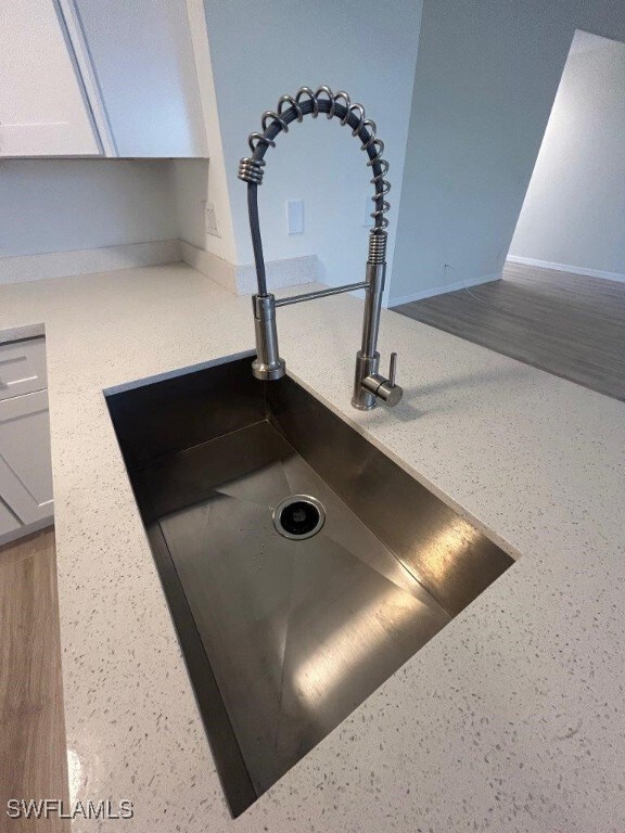 kitchen view of a sink, baseboards, light countertops, white cabinetry, and speckled floor