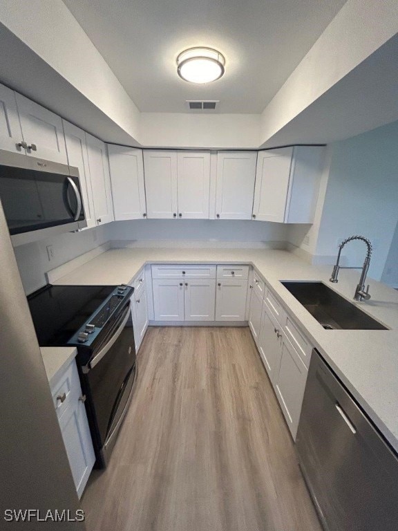 kitchen with appliances with stainless steel finishes, a sink, light wood-style floors, light countertops, and white cabinets