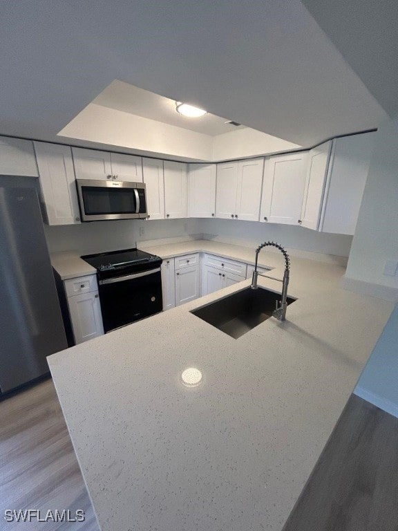 kitchen featuring light wood-type flooring, appliances with stainless steel finishes, sink, white cabinets, and kitchen peninsula