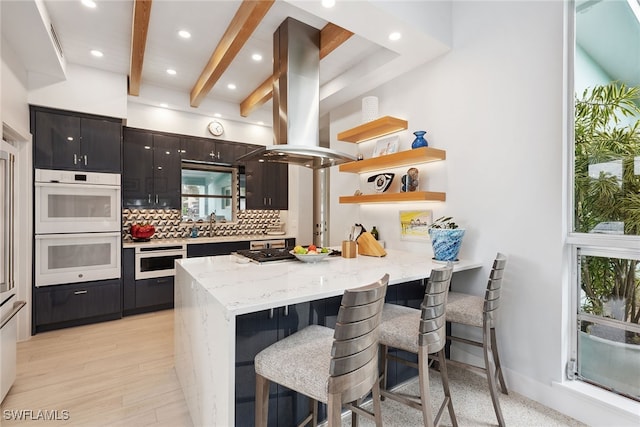 kitchen featuring a breakfast bar, white double oven, backsplash, kitchen peninsula, and island exhaust hood