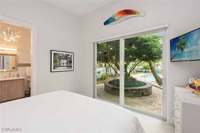 bedroom featuring ensuite bathroom, sink, access to exterior, light wood-type flooring, and a notable chandelier