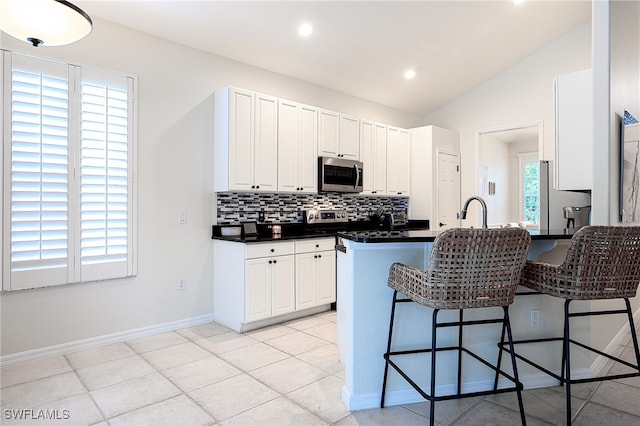 kitchen with stainless steel appliances, a wealth of natural light, white cabinets, kitchen peninsula, and lofted ceiling