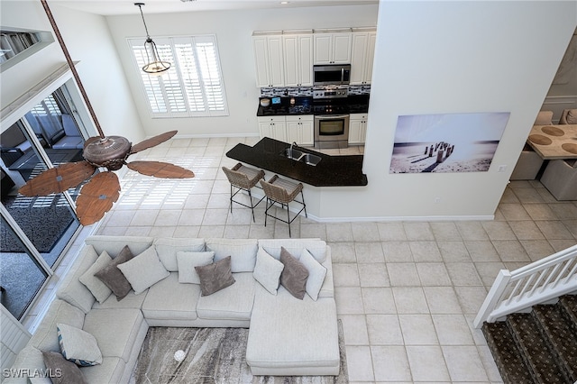 living room featuring sink, light tile patterned flooring, and ceiling fan with notable chandelier