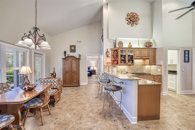 kitchen featuring stainless steel gas cooktop, hanging light fixtures, a breakfast bar area, high vaulted ceiling, and light stone countertops