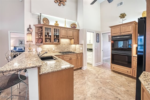 kitchen featuring black appliances, kitchen peninsula, light stone countertops, a kitchen bar, and a towering ceiling