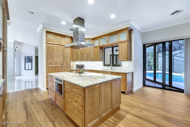 kitchen with decorative backsplash, ornamental molding, a kitchen island, light stone counters, and island exhaust hood