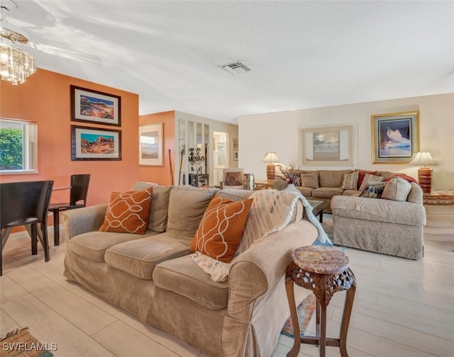 living room with light hardwood / wood-style floors, a textured ceiling, and an inviting chandelier