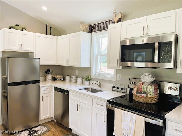 kitchen featuring stainless steel appliances, white cabinetry, sink, light wood-type flooring, and vaulted ceiling