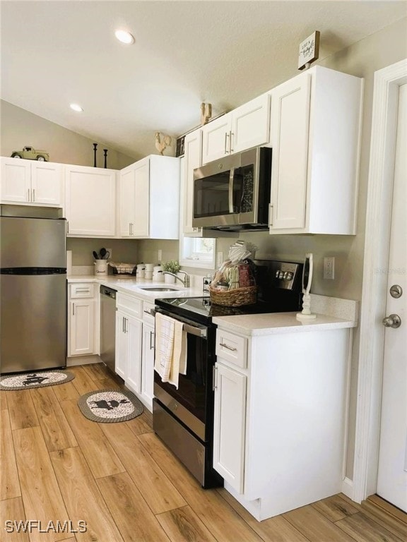 kitchen with stainless steel appliances, light hardwood / wood-style floors, white cabinetry, and vaulted ceiling