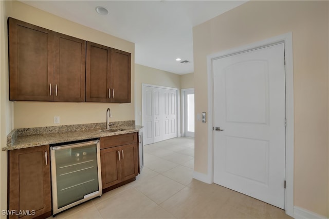 kitchen with light tile patterned floors, a sink, light stone countertops, beverage cooler, and baseboards