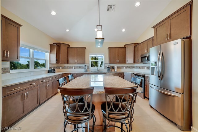 kitchen with a sink, a kitchen island, visible vents, hanging light fixtures, and appliances with stainless steel finishes