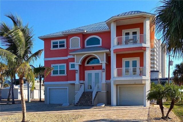 raised beach house with a garage, a balcony, metal roof, and stucco siding