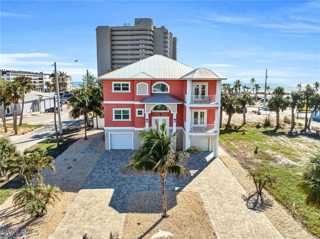 coastal home with a balcony, metal roof, an attached garage, decorative driveway, and stucco siding