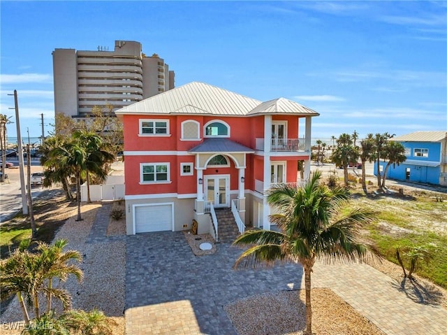 beach home featuring decorative driveway, metal roof, an attached garage, and stucco siding