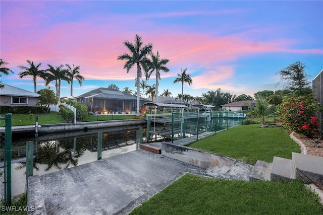 view of community with a dock, a water view, boat lift, and a lawn