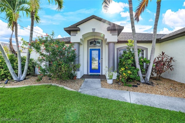 property entrance featuring a shingled roof, a yard, and stucco siding