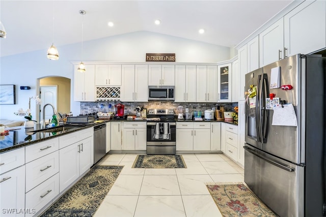 kitchen with stainless steel appliances, a sink, hanging light fixtures, dark stone countertops, and glass insert cabinets