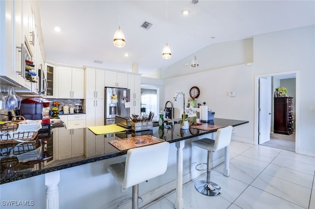 kitchen with a breakfast bar area, visible vents, white cabinets, stainless steel fridge, and glass insert cabinets