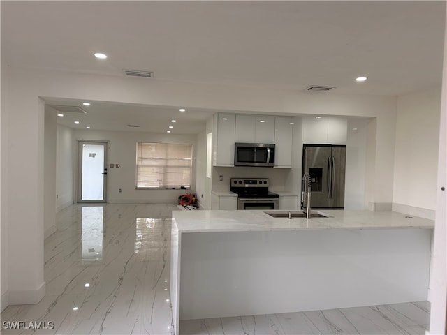 kitchen featuring sink, kitchen peninsula, appliances with stainless steel finishes, light stone countertops, and white cabinets