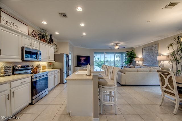 kitchen with a center island with sink, white cabinetry, appliances with stainless steel finishes, light tile patterned floors, and a kitchen bar