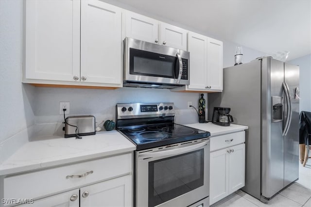 kitchen featuring white cabinets, stainless steel appliances, light tile patterned flooring, and light stone countertops